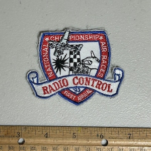 May include: A white, red, and blue embroidered patch with the text "National Championship Air Races" and "Radio Control First Annual 1983".