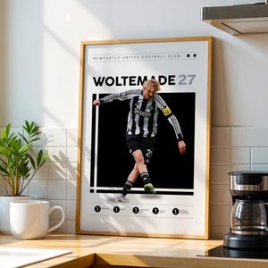 Puede incluir: Un póster enmarcado con un jugador de fútbol con una camiseta a rayas blancas y negras. El póster dice "WOLTEMADE 27" y "NEWCASTLE UNITED FOOTBALL CLUB". El jugador está capturado en acción sobre un fondo negro.