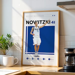 May include: A framed poster featuring a basketball player in a white and blue uniform. The poster has the text "DALLAS MAVERICKS" and "NOVITZKI 41". The player is pointing upwards with his right arm. The poster is in a wooden frame.
