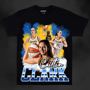 May include: Black t-shirt featuring a graphic of a basketball player, Caitlin Clark, with the text "Caitlin Clark" in blue and white. The graphic also includes a basketball and the text "Fever 22".