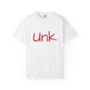 May include: White t-shirt with the word "Unk" in red, handwritten-style lettering across the front. The shirt has a crew neck and short sleeves. The fabric appears to be a soft, comfortable material.