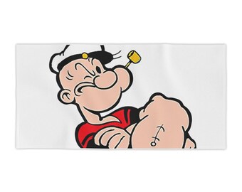 May include: White rectangular towel featuring a cartoon image of Popeye the Sailor Man. Popeye is depicted with a stern expression, wearing his signature sailor hat, red shirt, and holding his arm up to show off his muscular bicep.
