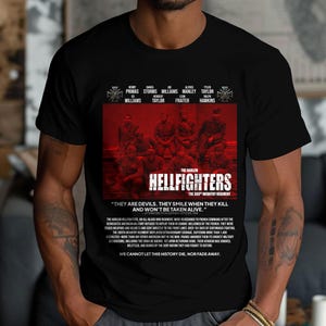 May include: Black t-shirt featuring a red graphic of the Harlem Hellfighters, the 369th Infantry Regiment, with text. The design includes the names of soldiers and the quote, "They are devils. They smile when they kill and won't be taken alive."