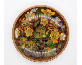 May include: A circular decorative dish with a floral pattern. The dish has a dark red base with yellow, green, and white flowers. The rim of the dish is light brown. The flowers are intricately detailed, creating a vibrant and eye-catching piece.