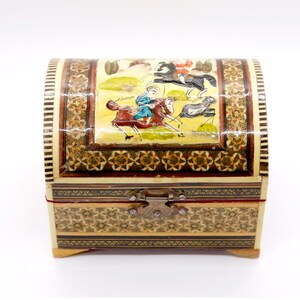 May include: A small, arched wooden chest with a hinged lid. The chest is adorned with intricate mosaic patterns and a painted scene of figures on horseback. The color palette includes beige, brown, red, and gold, with a metal clasp closure.