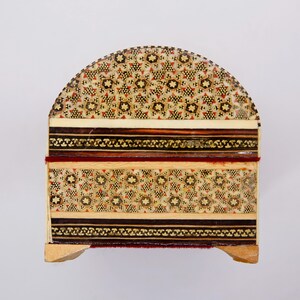 May include: A decorative wooden box with a domed lid. The box features intricate inlaid patterns in shades of beige, brown, and red. The design includes floral and geometric motifs, with a dark border and a red accent.