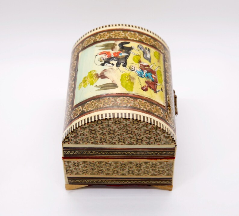 May include: A decorative, arched-top box with intricate mosaic and painted details. The box features a colorful scene on the curved lid, with figures and foliage. The box is approximately 6 inches long, 4 inches wide, and 4 inches tall.