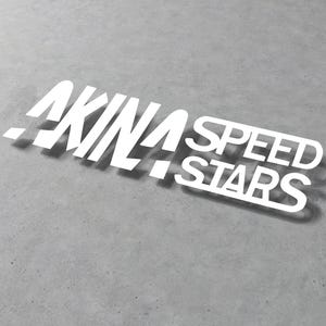 Può includere: Adesivo in vinile bianco con il testo "AKINA SPEED STARS" in un carattere audace e stilizzato.