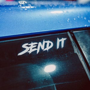 May include: A blue car with a white sticker on the rear window that says "SEND IT".