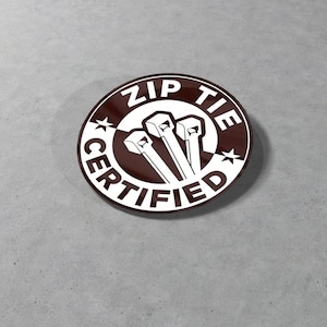 Puede incluir: Una pegatina blanca con un círculo marrón y el texto "ZIP TIE CERTIFIED" en blanco. Se muestran tres bridas de plástico blancas en el centro del círculo.