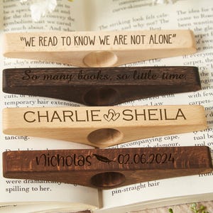 May include: Four wooden bookends with personalized engravings. The top bookend reads "We read to know we are not alone". The second bookend reads "So many books, so little time". The third bookend reads "Charlie Sheila" with two hearts. The bottom bookend reads "Nicholas 02.06.2024" with a feather.