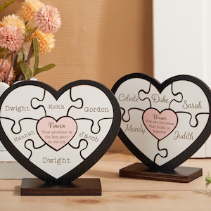 May include: Two wooden heart-shaped puzzle pieces with names and a message. The top piece reads "Celeste Duke Sarah Mandy Mum You are the piece that holds us together Judith". The bottom piece reads "Dwight Keith Gordon Jacob Nana Your presence is the key piece to our joy Dwight Hannan".