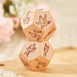 Puede incluir: Dos dados de madera con diferentes imágenes de parejas en varias posiciones. Los dados están apilados uno encima del otro.