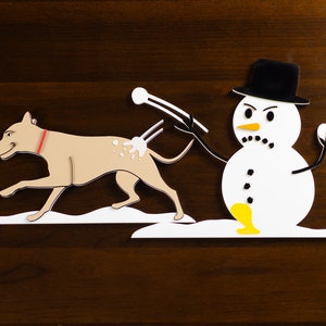 May include: A white snowman with a black top hat and a yellow carrot nose throws a snowball at a brown dog with a red collar.