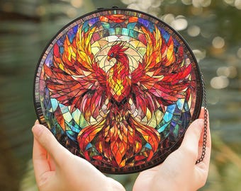 May include: A stained glass suncatcher featuring a colorful phoenix with red, orange, yellow, and blue hues. The phoenix is surrounded by a circular frame with a black chain.