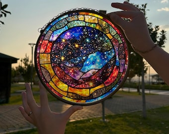 May include: A stained glass window depicting a colorful galaxy with stars and a mountain range. The window is round and has a metal frame.