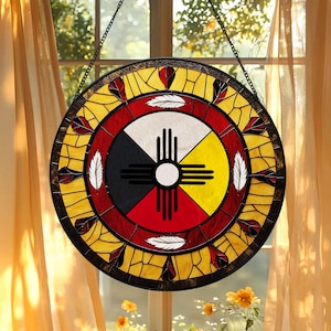 May include: A circular stained glass suncatcher featuring a central Zia sun symbol in black against four quadrants of white, yellow, red, and black. The design is surrounded by a red ring and an outer border of yellow glass with feather motifs.