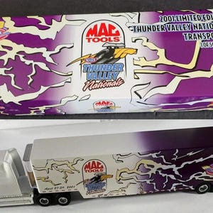 May include: A die-cast model of a white and silver semi-truck with a trailer, featuring the "MAC TOOLS" and "Thunder Valley Nationals" logos. The box above is purple and white with the text "2001 Limited Edition Transporter of 5000 Pieces."