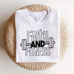 Może przedstawiać: Biała koszulka z czarnym napisem "Faith and Fitness" i grafiką hantle.