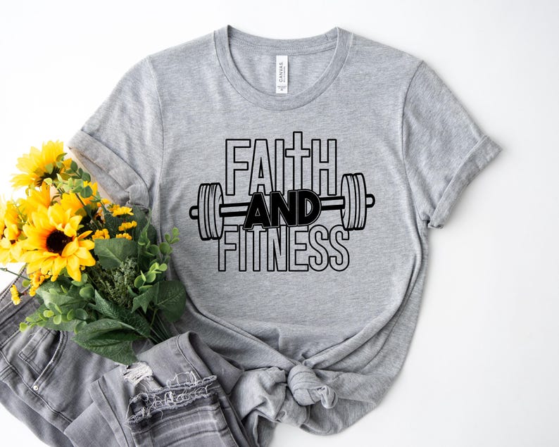 Może przedstawiać: Szara koszulka z czarnym napisem "Faith and Fitness" i grafiką sztangi.
