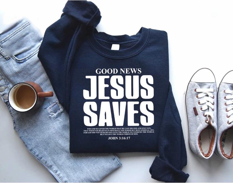 May include: A navy blue sweatshirt with the text "GOOD NEWS JESUS SAVES" in white. The text is in a bold, blocky font. Below the text is a Bible verse from John 3:16-17.