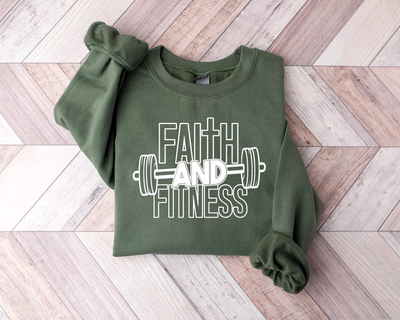 Może przedstawiać: Zielona bluza z napisem "Faith and Fitness" w białym kolorze i grafiką białej sztangi.