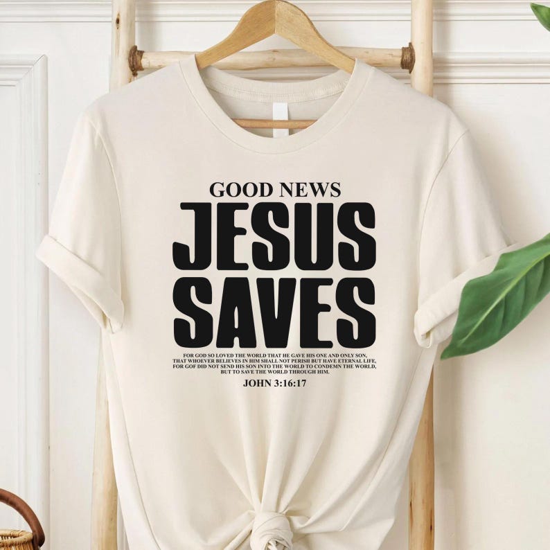 May include: A beige t-shirt with the text "GOOD NEWS JESUS SAVES" in black. The shirt also includes a bible verse from John 3:16-17.