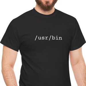 Pode incluir: Uma camiseta preta com o texto "/usr/bin" impresso em branco na frente.