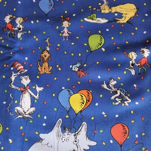 May include: A blue fabric with a repeating pattern of characters from the book "The Cat in the Hat". The characters include the Cat in the Hat, Thing 1 and Thing 2, the Lorax, and the Grinch. The fabric is covered in confetti.