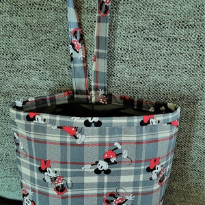 May include: A gray and white plaid tote bag with a handle, featuring a repeating pattern of Mickey and Minnie Mouse. The bag has a black interior and red accents in the plaid design.
