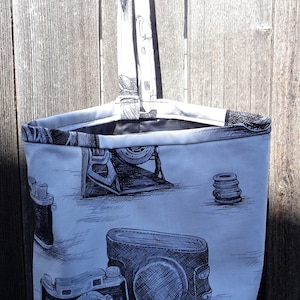 May include: A gray canvas tote bag with a black handle. The bag has a design of vintage cameras printed on it.