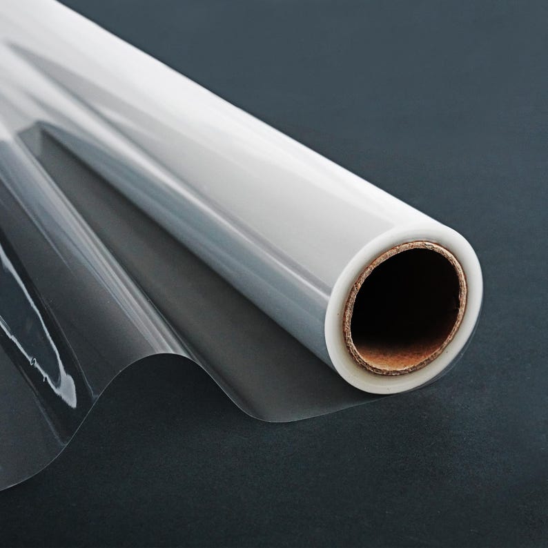 May include: A roll of clear cellophane wrapping paper on a black background. The paper is rolled up and the end of the roll is visible.