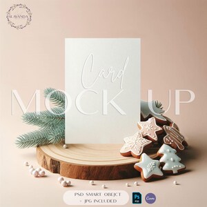 May include: A blank white card with the word "Card" embossed on it, displayed on a wooden slice with festive gingerbread cookies. The scene includes a sprig of evergreen and decorative pearls, with the text "MOCK UP".