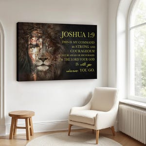 Può includere: Una stampa su tela raffigurante la faccia di un leone con una corona di spine su un lato. Il testo "JOSHUA 1:9" e una citazione motivazionale sono visualizzati in lettere dorate. L'opera d'arte è appesa a una parete bianca, sopra uno sgabello di legno e una poltrona color crema.