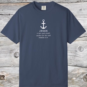 Könnte beinhalten: Ein marineblaues T-Shirt mit einem weißen Anker-Motiv und dem Text "JESUS a sure and steady anchor for the soul HEBREWS 6:19". Das Shirt besteht aus einem weichen, bequemen Material.