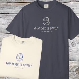 May include: Two t-shirts, one cream and one navy blue, with the text "WHATEVER IS LOVELY" and a seashell graphic. The text "Philippians 4:8" is below the main text. Both shirts have a crew neck and short sleeves.