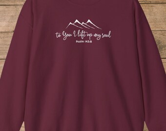 May include: A maroon sweatshirt with white text and mountain graphic. The text reads "to You I lift up my soul" with "Psalm 143:8" below. The sweatshirt is made of a soft material.