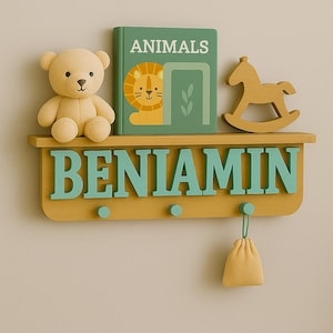 Peut inclure: Une étagère en bois avec le nom "BENJAMIN" en lettres turquoise. Elle présente un ours en peluche, un livre intitulé "ANIMAUX" avec un lion et un cheval à bascule en bois. Un petit sac jaune est suspendu en dessous.