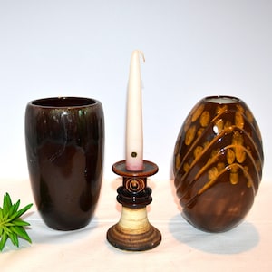 May include: Three ceramic vases in brown and green glaze. The vase on the left is tall and cylindrical. The vase on the right is round and has a wavy design. The vase in the center is a candle holder with a white candle.