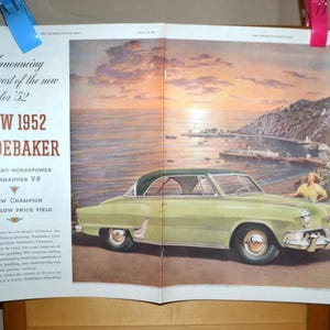May include: An advertisement for the 1952 Studebaker Commander V8. The illustration shows a light green car with a dark green roof parked near a coastal town. The ad includes the text "Announcing the newest of the new for '52".