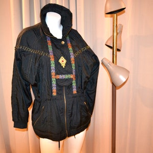 May include: A black quilted jacket with a gold zipper and colorful trim. The jacket has a gold brooch with a floral design.