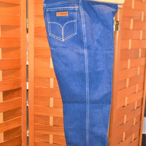 May include: A pair of blue denim jeans hanging on a wooden hanger. The jeans have a brown leather patch with the word "G-Star" on it.