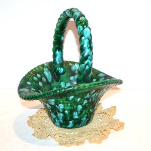 May include: A green ceramic basket with a twisted handle. The basket has a woven pattern and is decorated with white speckles.