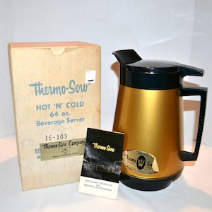 May include: A gold Thermo-Sew 64 ounce hot and cold beverage server with a black lid and handle. The server is in its original box with the text "Thermo-Sew Hot 'N' Cold 64 oz. Beverage Server 16-103 Thermo-Serv Company Anoka, Minnesota 55303" printed on the box.