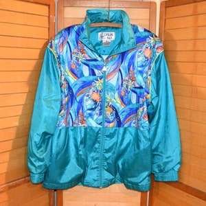 May include: A teal blue windbreaker jacket with a colorful abstract print on the front. The jacket has a zipper closure and a stand-up collar. The brand label reads "Casual Isle".