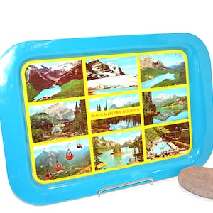 Puede incluir: Una bandeja rectangular con un borde azul brillante y un interior amarillo con nueve imágenes escénicas de las Montañas Rocosas canadienses. La bandeja incluye el texto "THE CANADIAN ROCKIES".