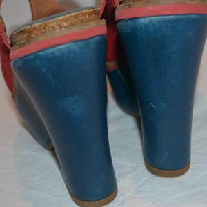 May include: Blue wedge sandals with red accents and a cork footbed. The sandals have a wedge heel and a strap. The heel height is approximately 4 inches.