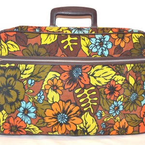 Könnte beinhalten: Vintage Koffer mit braunem Griff und Reißverschluss. Der Koffer ist mit einem Blumenmuster mit orangefarbenen, gelben, blauen und braunen Blumen und Blättern bedeckt. Der Koffer hat eine rechteckige Form.