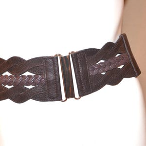 Puede incluir: Cinturón ancho de cuero marrón oscuro con un detalle central trenzado. El cinturón tiene un diseño de borde festoneado y un cierre metálico. El cinturón mide unos 10 cm de ancho.