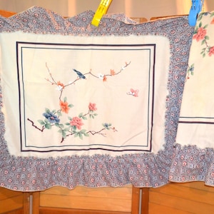 Könnte beinhalten: Ein rechteckiger Kissenbezug und ein passendes flaches Stoffstück mit cremefarbenem Untergrund und einem zentralen Blumen- und Vogelmotiv. Das Design zeigt blaue und orangefarbene Blüten, einen kleinen blauen Vogel und rosa Schmetterlinge mit blauem Rand.